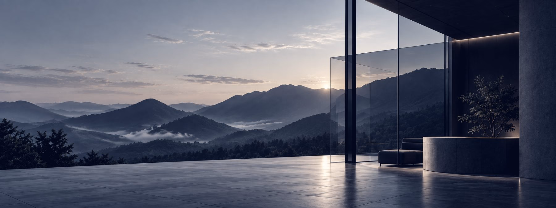 A quiet lounge with floor-to-ceiling glass looking out over mountains at dusk